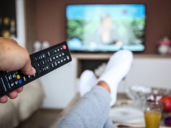 TV in background with person's socked feet and a remote control in foreground